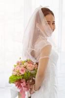 An Asian bride wore a white wedding dress, standing, holding a bouquet of beautiful flowers behind her. photo