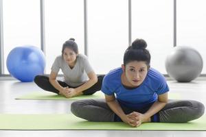 dos mujeres asiáticas de mediana edad haciendo yoga sentadas en una alfombra de goma en un gimnasio. foto