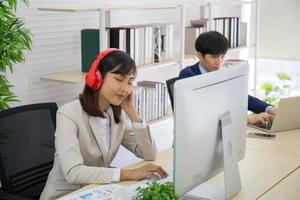 mujeres de negocios asiáticas escuchando música con auriculares en la oficina. foto