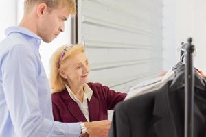 An elderly female designer is explaining information to customers about male suits. photo