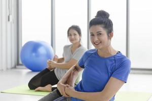 dos mujeres asiáticas de mediana edad haciendo yoga sentadas en una alfombra de goma en un gimnasio. foto