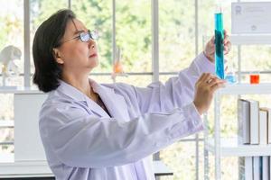 Discovering a cure for an Asian female scientist who is concentrated, holding a test tube and watching while working. photo