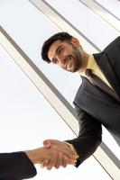 dos jóvenes empresarios están bien vestidos con traje y corbata, tomados de la mano, mostrando negocios separados con caras felices y sonrientes. foto