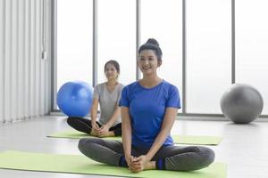 Two middle-aged Asian women doing yoga sitting on a rubber mat in a gym. photo