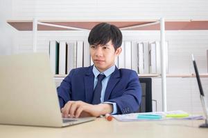 A young Asian businessman sat seriously on the desk in the office. photo