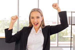 una hermosa mujer de negocios con traje, bien vestida, sentada en la oficina, emocionadamente feliz, levantó la mano con una sonrisa brillante sobre la mesa foto