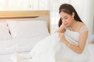 una novia asiática con un vestido de novia blanco se arrodilla en la cama con su pañuelo para absorber sus lágrimas. foto