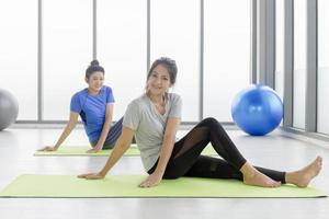 Two middle-aged Asian women are doing rubber mat yoga in the gym.
