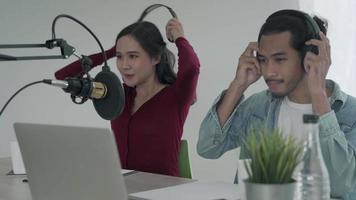 woman was speaking on a morning radio station broadcasting a news program and men preparing the content via computers. The woman is testing the microphone by speaking test. concept podcast . video