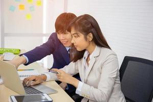 A young professional Asian businesswoman who uses a laptop computer and a credit card to pay online while sitting at her desk, with a male friend next to him. photo