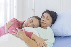 una mujer asiática abraza a su madre que se está recuperando en una cama de hospital. foto