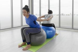 dos mujeres asiáticas de mediana edad haciendo yoga sentadas en una pelota de goma en el gimnasio. foto