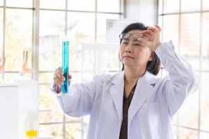 Discovering a cure for an Asian female scientist who is concentrated, holding a test tube and watching while working. photo