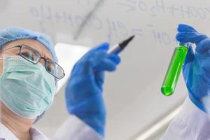 una científica asiática está escribiendo la fórmula para calcular la química en vidrio transparente en un laboratorio. foto