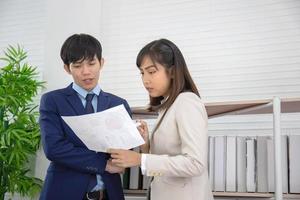 Two Asian businessmen and women stand together in the office in the hand holding the documents. photo