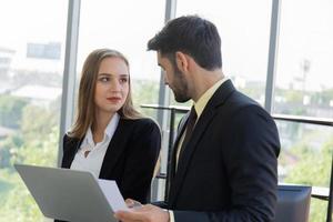 Two business men and women were neatly dressed in a suit and tie standing meeting beside the glass wall in the office. photo