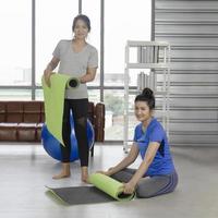 Two middle-aged Asian women roll up a rubber mat for yoga after finishing exercising indoors. photo
