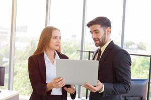 Two business men and women were neatly dressed in a suit and tie standing meeting beside the glass wall in the office. photo