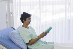 The elderly Asian women sat on the bed to read in the hospital. photo