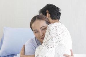 A young Asian woman who is sick in a hospital embraces her mother who looks after her. photo