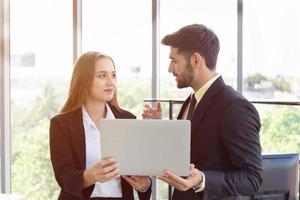 Two business men and women were neatly dressed in a suit and tie standing meeting beside the glass wall in the office. photo