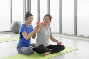 las entrenadoras están enseñando a las clientas asiáticas de mediana edad a hacer ejercicio haciendo pesas en el gimnasio. foto