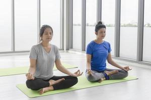 Two middle-aged Asian women doing yoga sitting on a rubber mat in a gym. photo