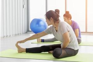 Two middle-aged Asian women doing yoga sitting on a rubber mat in a gym. photo