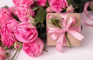 rosas frescas de color rosa pastel y cajas de regalo envueltas en papel kraft con cintas sobre una mesa de madera blanca. foto