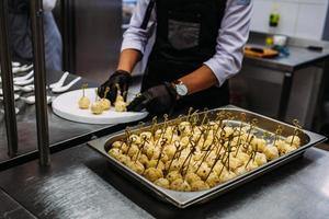 A cook in black gloves prepares catering cheese balls. photo