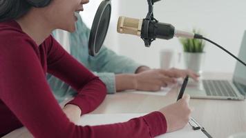 Aziatische radiopresentator podcast in studio. mannelijke en vrouwelijke sprekers praten via microfoons en camera's op hun computers. video