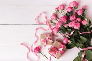 rosas frescas de color rosa pastel y cajas de regalo envueltas en papel kraft con cintas sobre una mesa de madera blanca. foto