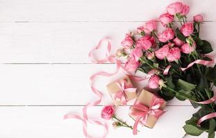 rosas frescas de color rosa pastel y cajas de regalo envueltas en papel kraft con cintas sobre una mesa de madera blanca. foto