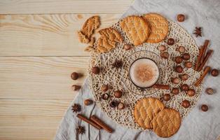 Hot cocoa with cookies, cinnamon sticks, anise, nuts on wooden background. photo