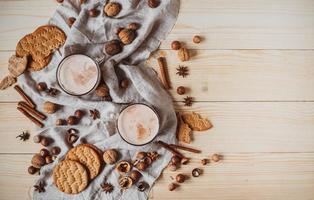 Hot cocoa with cookies, cinnamon sticks, anise, nuts on wooden background. photo