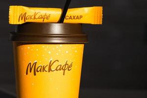 Coffee to go of McDonald's with the inscription Maccafe in Russian stick with sugar on the table with a napkin and a straw. Fast food restaurant chains. Russia, Kaluga, March 21, 2022.