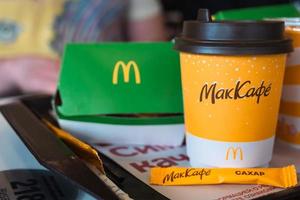 A paper cup of McDonald's coffee with the inscription Maccafe in Russian and a hamburger in a box on a tray. Fast food restaurant chains. Russia, Kaluga, March 21, 2022. photo