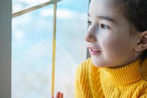 A girl in a yellow sweater looks out the window. Childhood dreams, a look into the future. Copy space photo