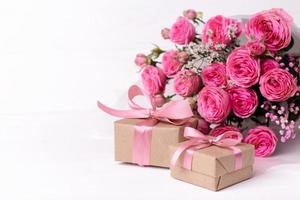 Fresh pastel soft pink roses, and gift boxes wrapped in kraft papper with ribbons on white wooden table. photo