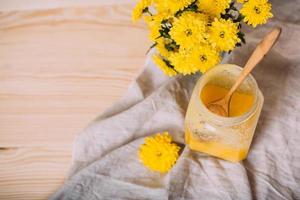 A jar of solid honey and flowers on wooden background.