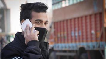 Young man holding mobile phone, using smartphone, making a call, talking on the phone, standing on street with transport traffic on the background photo