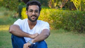 joven indio guapo sentado en el parque al aire libre disparar foto