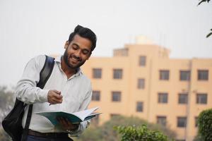 joven estudiante universitario masculino parado afuera en el campus y leyendo un libro foto