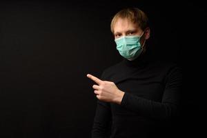 A man in black clothes on a black background in a protective mask is selling your product. photo