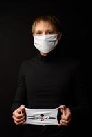 A man in black clothes on a black background holds in his hand a protective mask for the child. photo