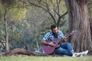 young boy with his guitar and playing guitar in park photo