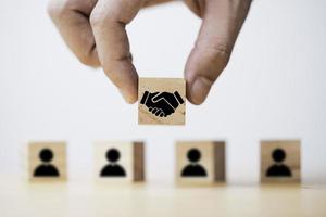 Hand holding wooden cube which drawing of hand shaking print screen on wooden cube block  in front of human icon for business deal and agreement concept. photo