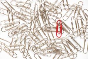 Red paper clip show different from the others on white background photo