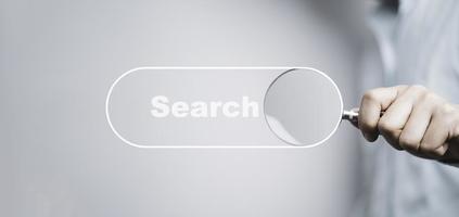mano que sostiene la lupa con el icono de la barra de búsqueda para la optimización del motor de búsqueda o el concepto seo. foto