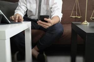 contexto de justicia y derecho.abogado sentado en el sofá y trabajando con un teléfono inteligente,teclado de conexión de una tableta digital con mazo y documento en la mesa de estar en casa foto